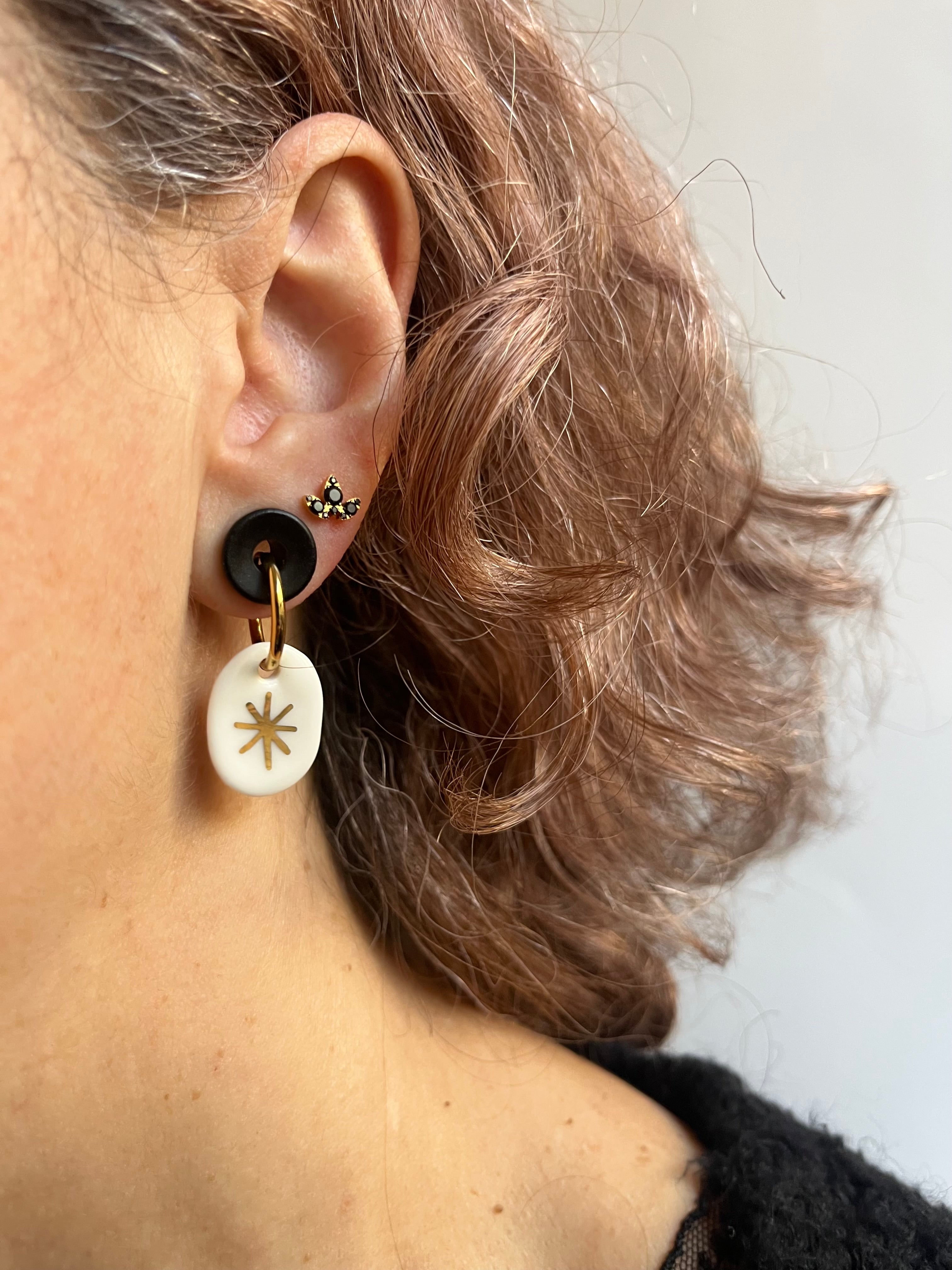 boucle d'oreille dorée avec son charm ovale en porcelaine blanche émaillée, avec un motif d'étoile céleste à l'or fait main