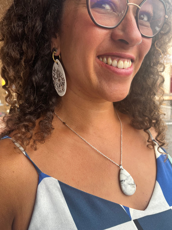 Boucle d'oreille pendante ovale en porcelaine blanche Matilou, avec illustration style tatouage rock "LOVE" et or pur, portée avec le sourire par une cliente.