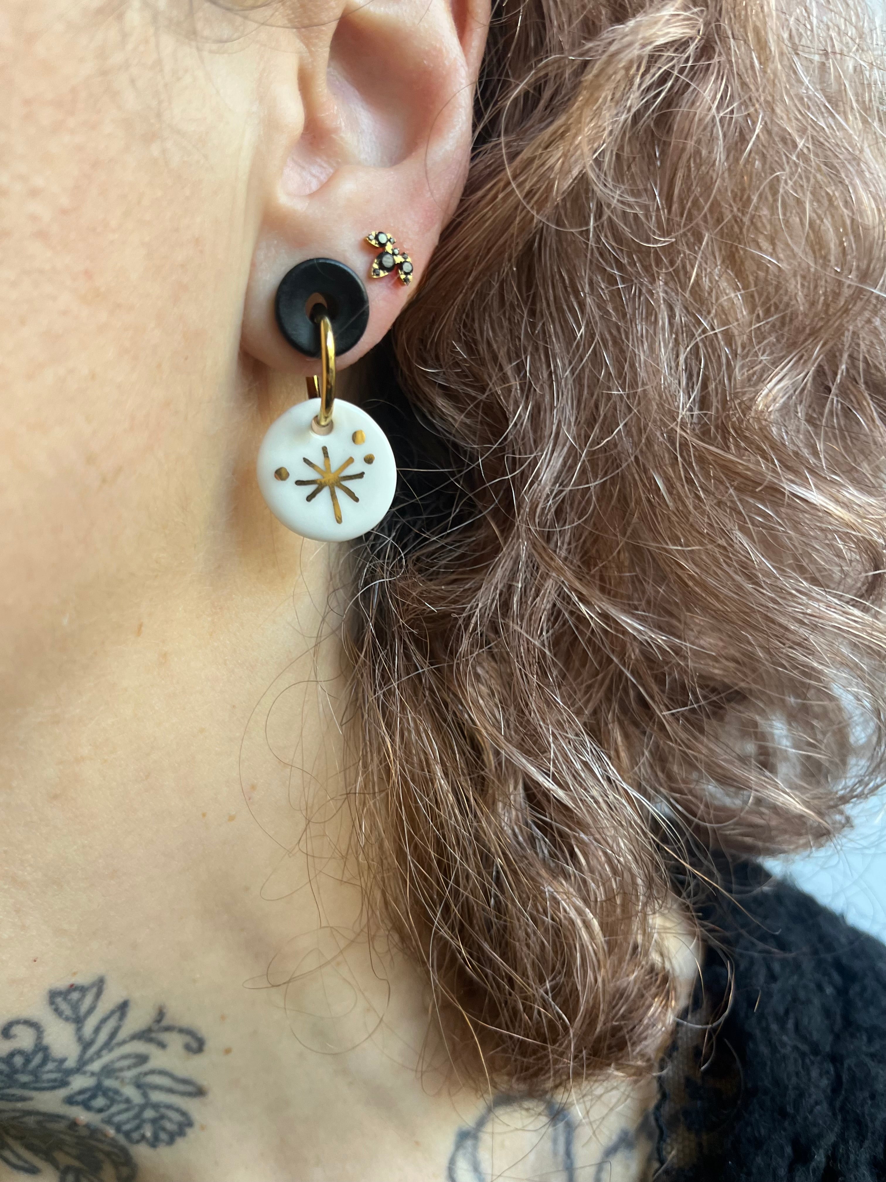 boucle d'oreille ronde en porcelaine blanche émaillée, avec un motif d'étoile qui brille dorée à l'or fin liquide à la main. .