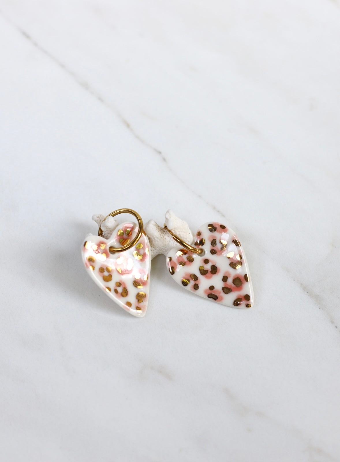 Paire de boucles d'oreilles dorées avec grands pendants en porcelaine émaillée blanche en forme de cœur, décorés d'un motif léopard rose pastel et taches d'or fin