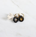 Une paire de boucles d'oreilles dorées avec des pendentifs noirs ornés d'un motif étoile dorée au centre