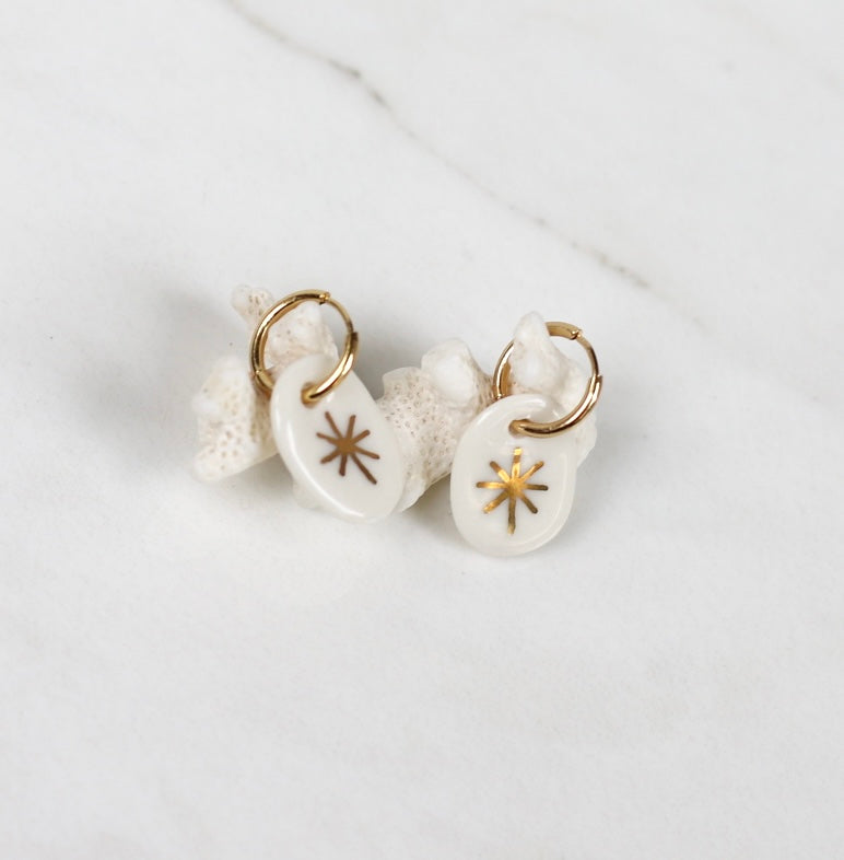 boucles d'oreilles pendantes en porcelaine blanche, ornés d'une étoile rayonnante peinte à l'or fin.