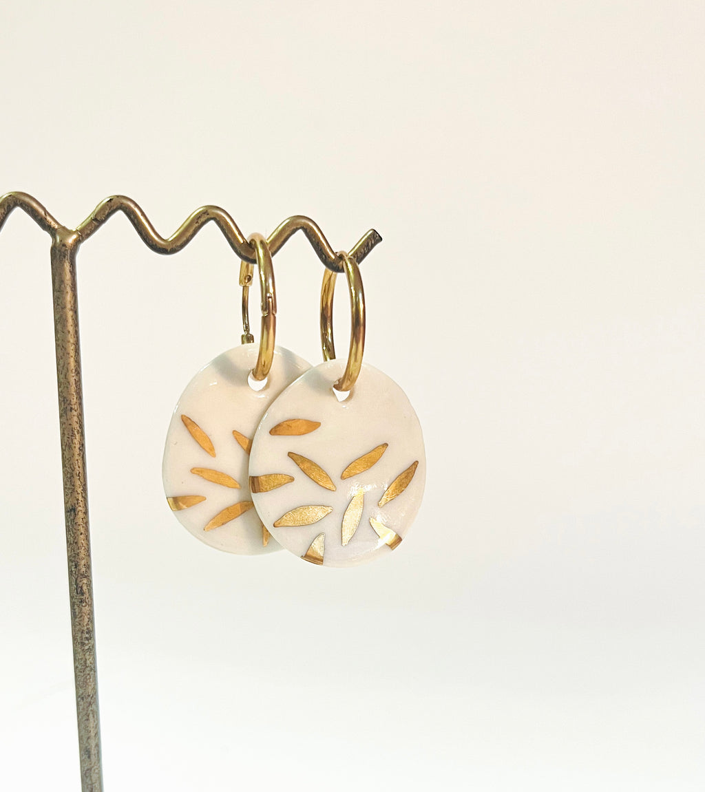 Boucles d'oreilles en or en porcelaine blanche émaillée, illustrant un motif graphique floral doré peint à la main.