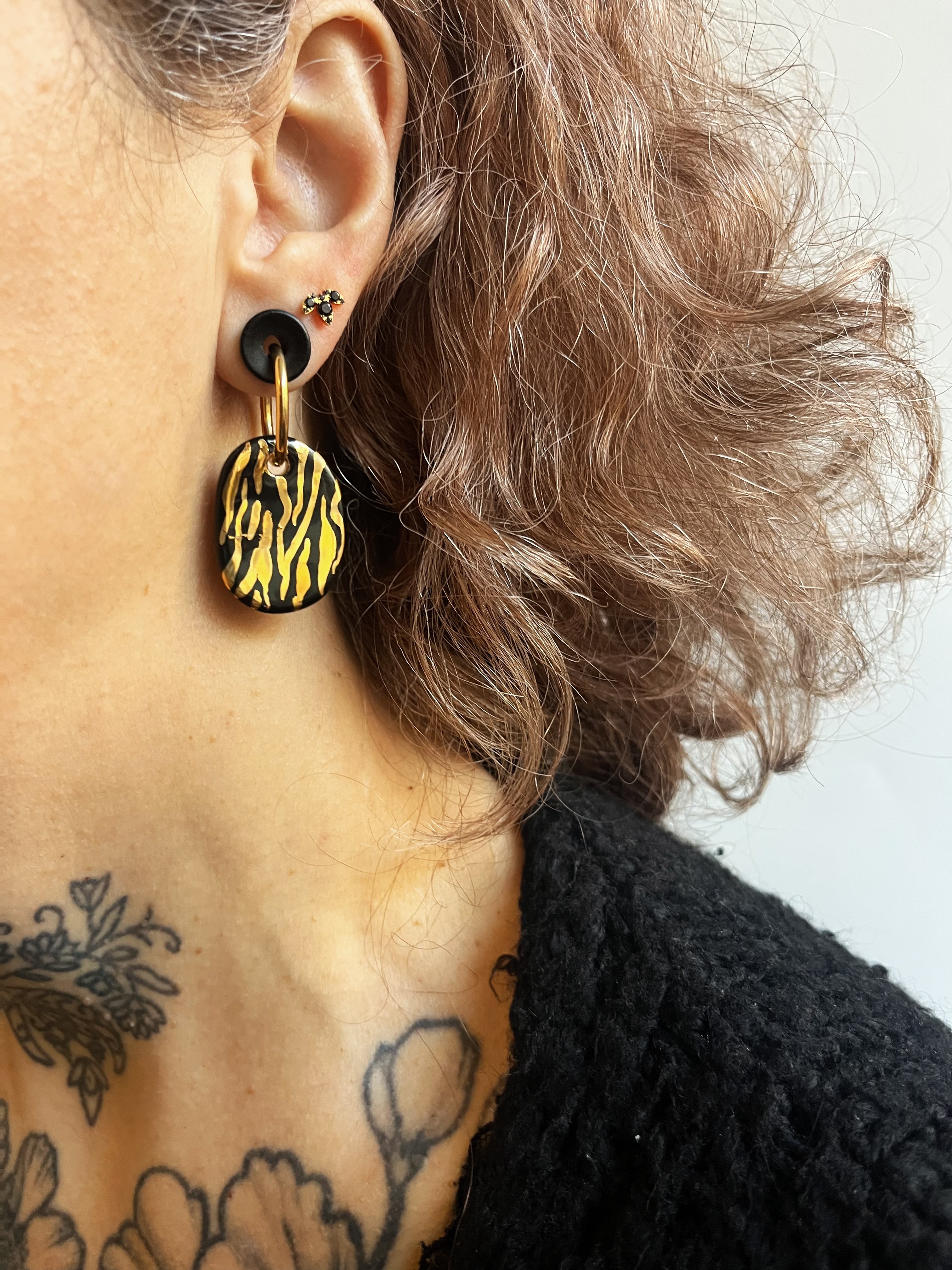 boucles d'oreilles anneaux dorés avec des charms ovales en porcelaine noire et un motif animalier zébré à l'or liquide peint à la main 