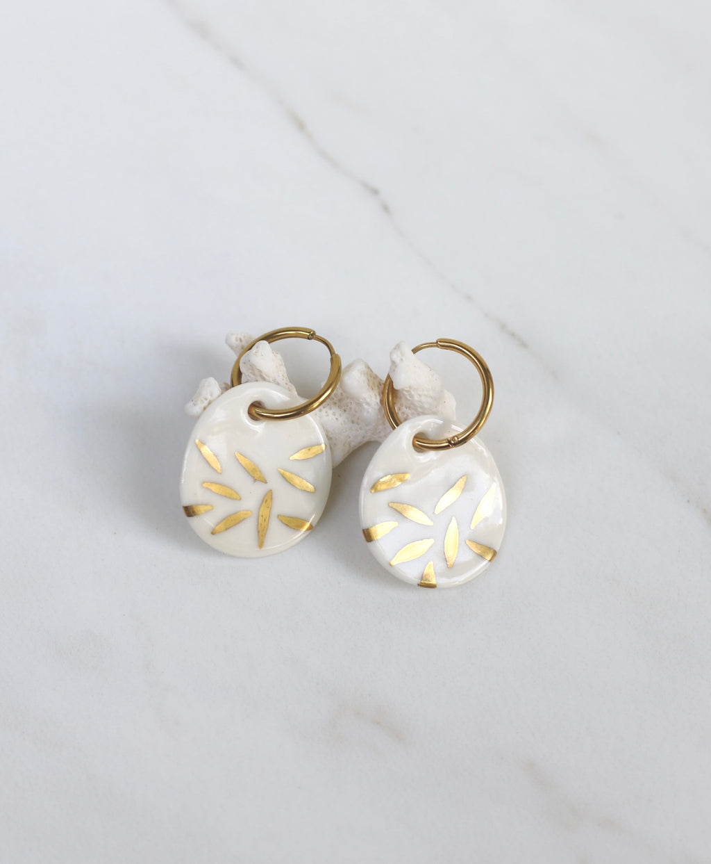 Paire de boucles d'oreilles dorées avec médaillons pendants de forme ovale en porcelaine blanche, ornés de motif floral d'or.