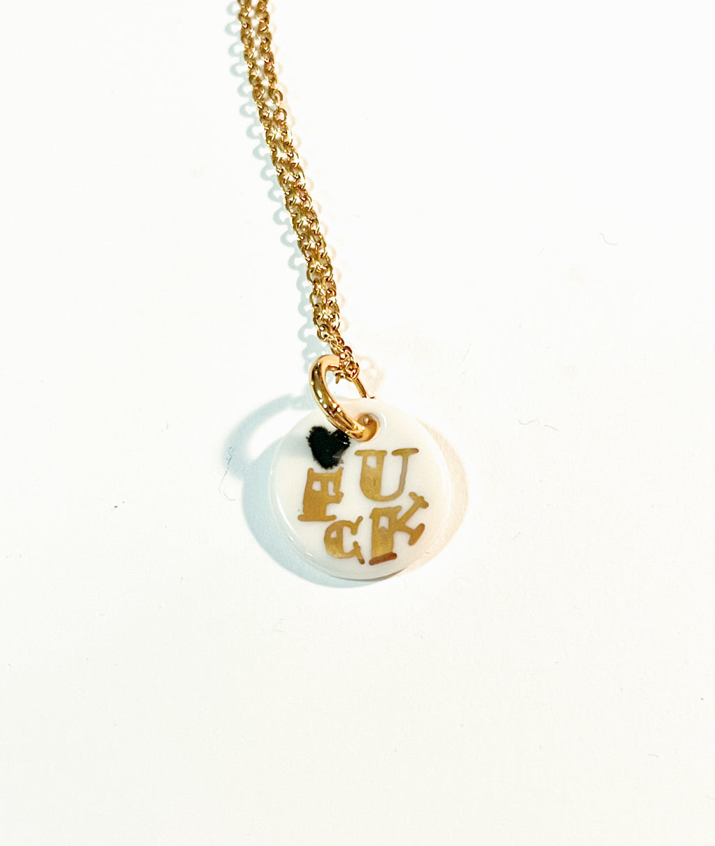 collier médaille FUCK en porcelaine blanche et or, détaillé de lettres dorées peintes à la main et avec un mini cœur noir.