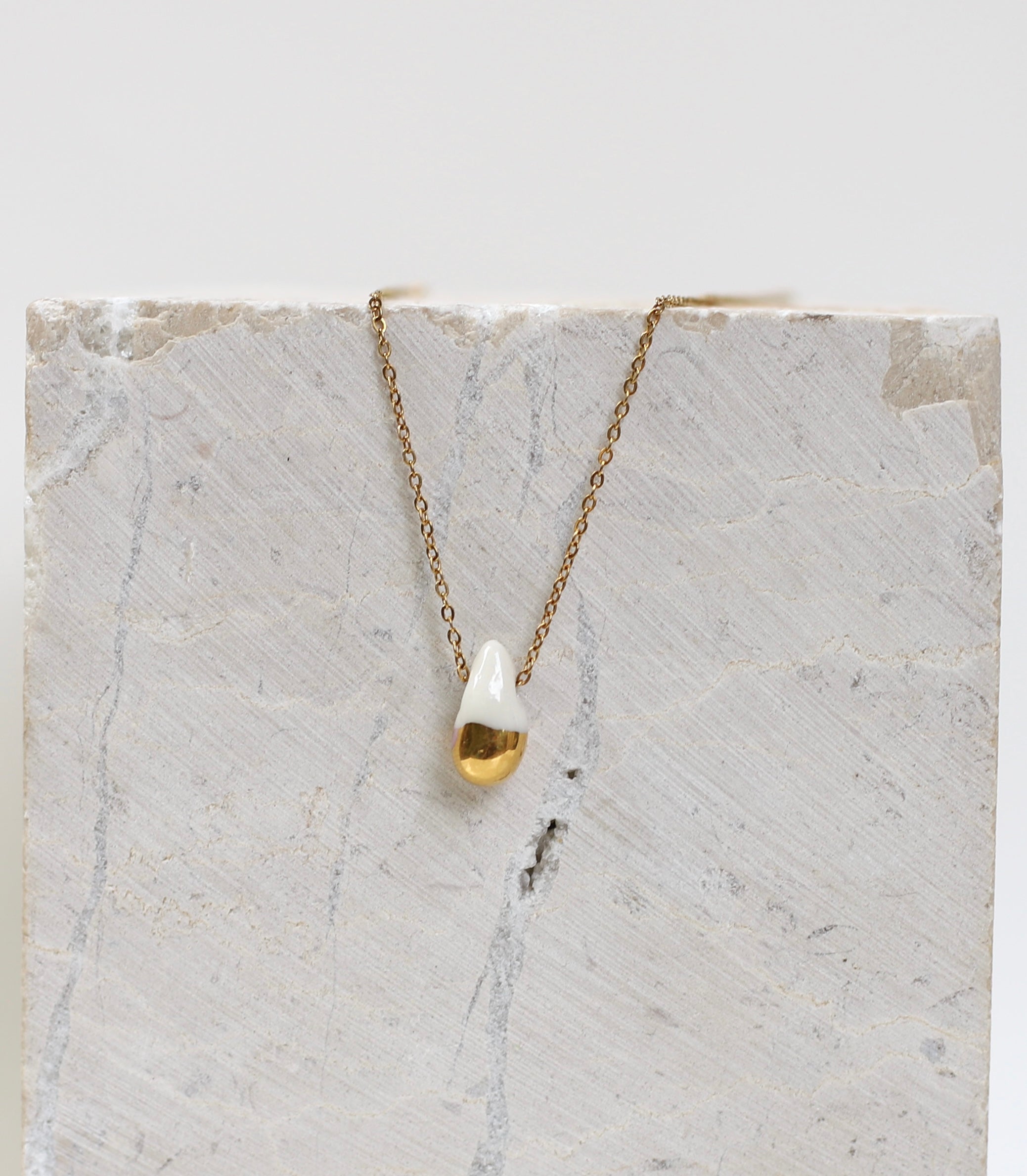 Collier fin  doté d'un pendentif en forme de goutte en porcelaine blanche dont la partie inférieure est recouverte d'or fin brillant.