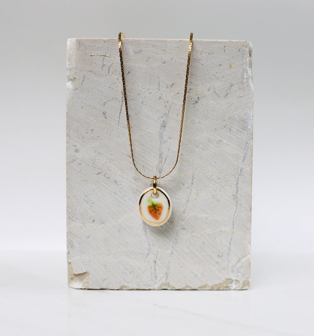 collier en porcelaine blanche, avec comme motif une fraise peint à la main avec des détails à l'or. fait main à lyon.