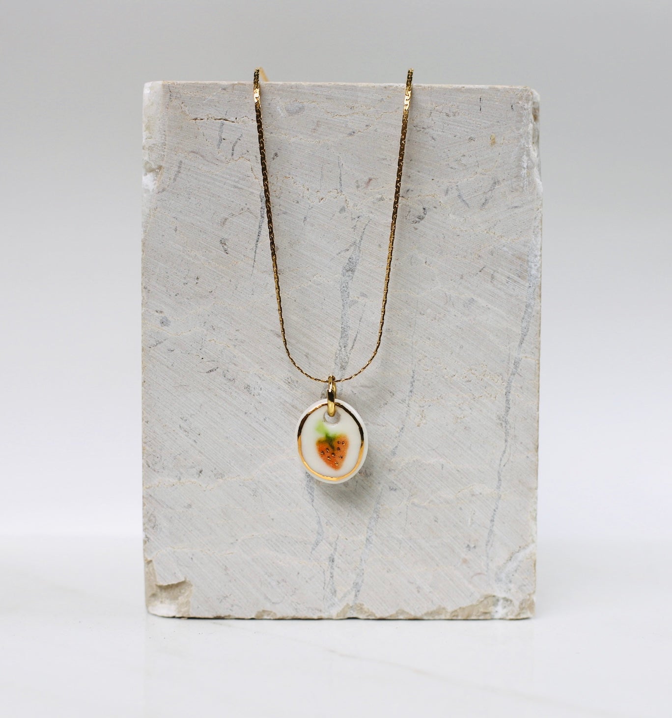 collier en porcelaine blanche, avec comme motif une fraise peint à la main avec des détails à l'or. fait main à lyon.