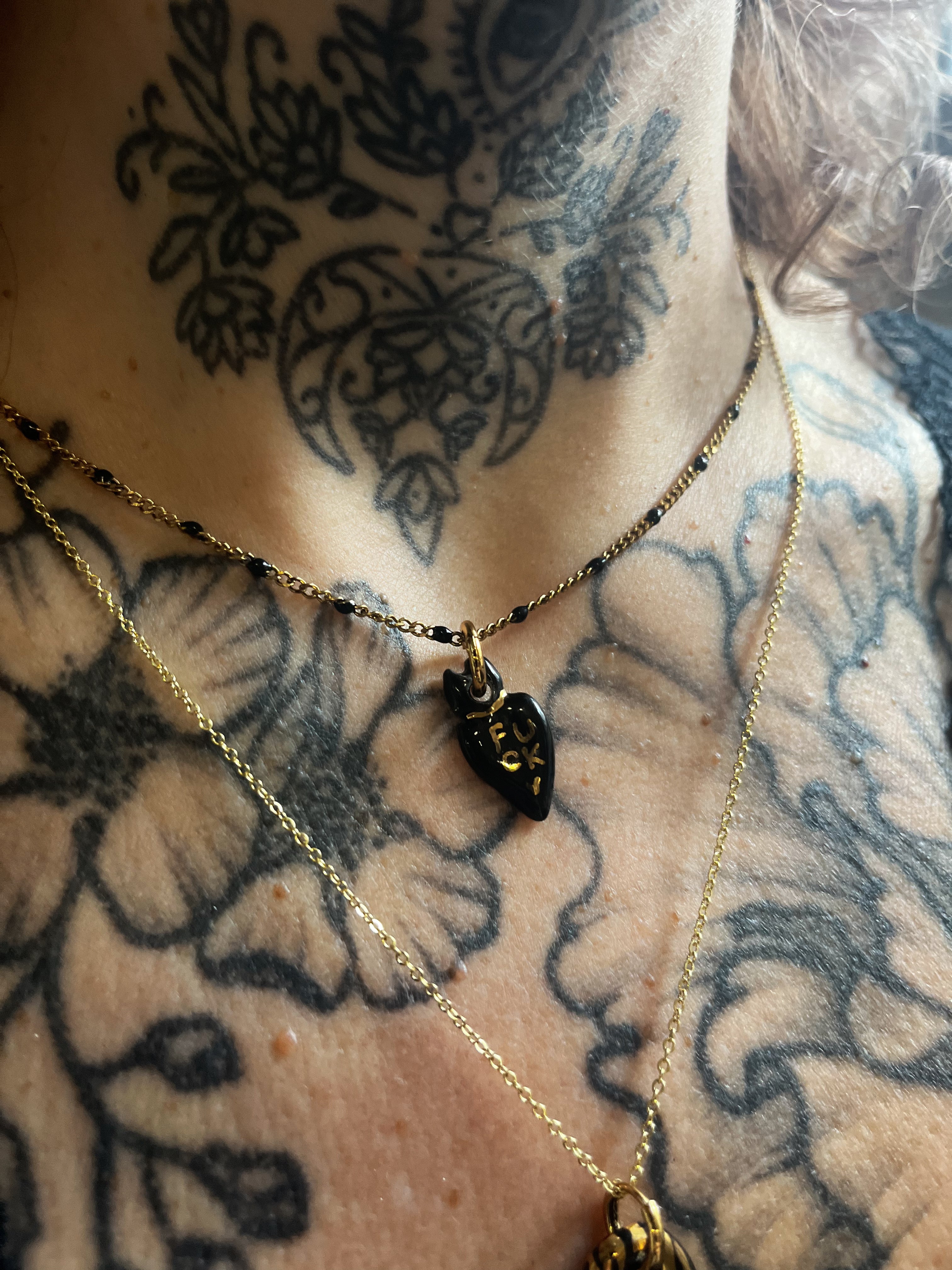 un collier composé d'un petit cœur en porcelaine noire portant l'inscription rock FUCK peinte à la main à l'or liquide.