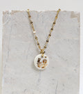 Collier délicat pour femme avec une médaille ronde en porcelaine blanche émaillée, affichant le mot LOVE peint à la main en lettres d'or fin