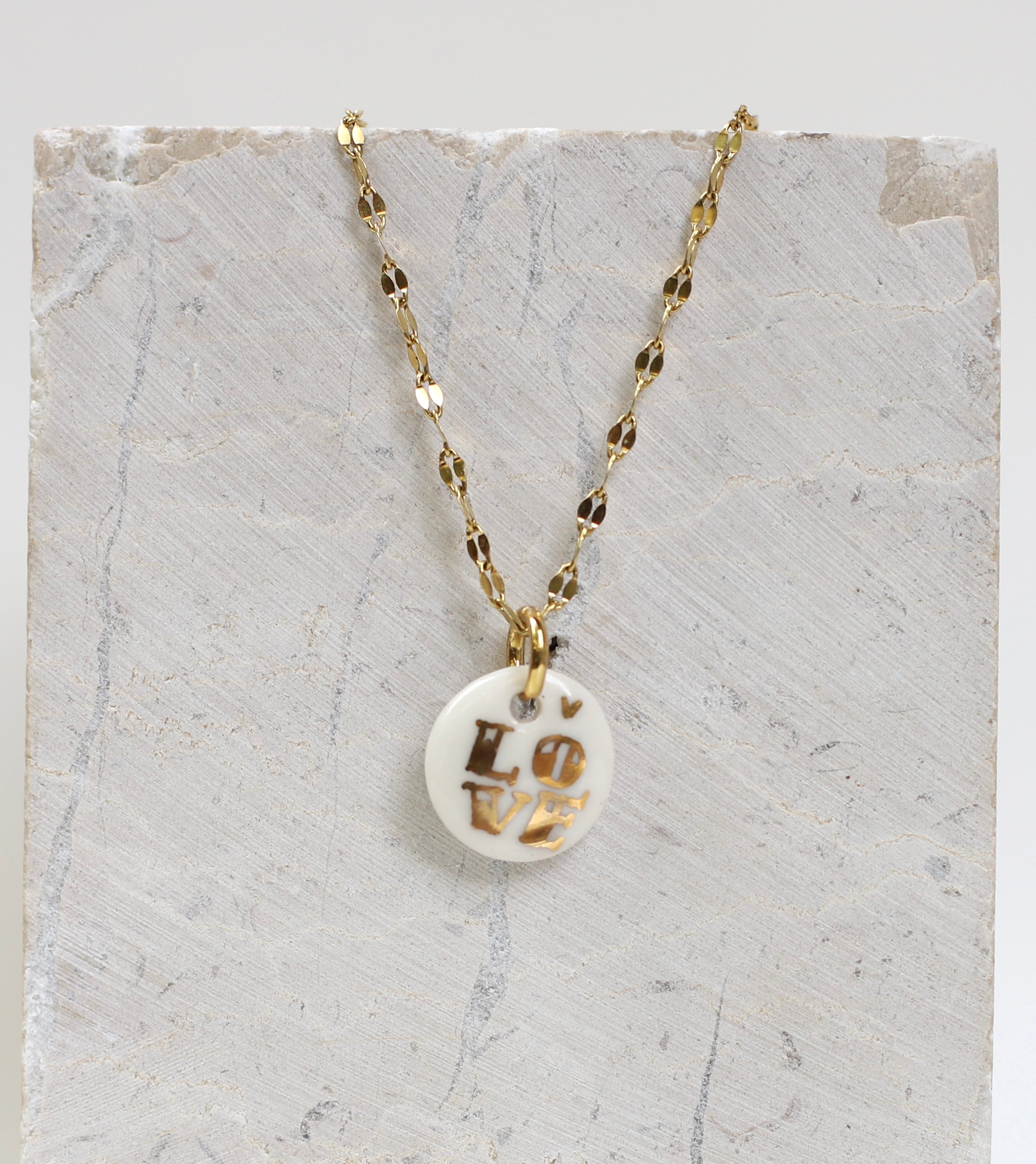 Collier délicat pour femme avec une médaille ronde en porcelaine blanche émaillée, affichant le mot LOVE peint à la main en lettres d'or fin