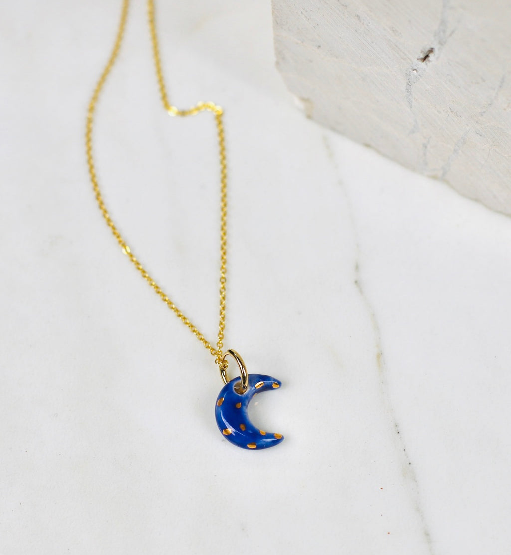 collier Céleste, avec un pendentif artisanal en porcelaine émaillée orné d'un motif lune bleu nuit et d'étoiles dorées peintes à la main.