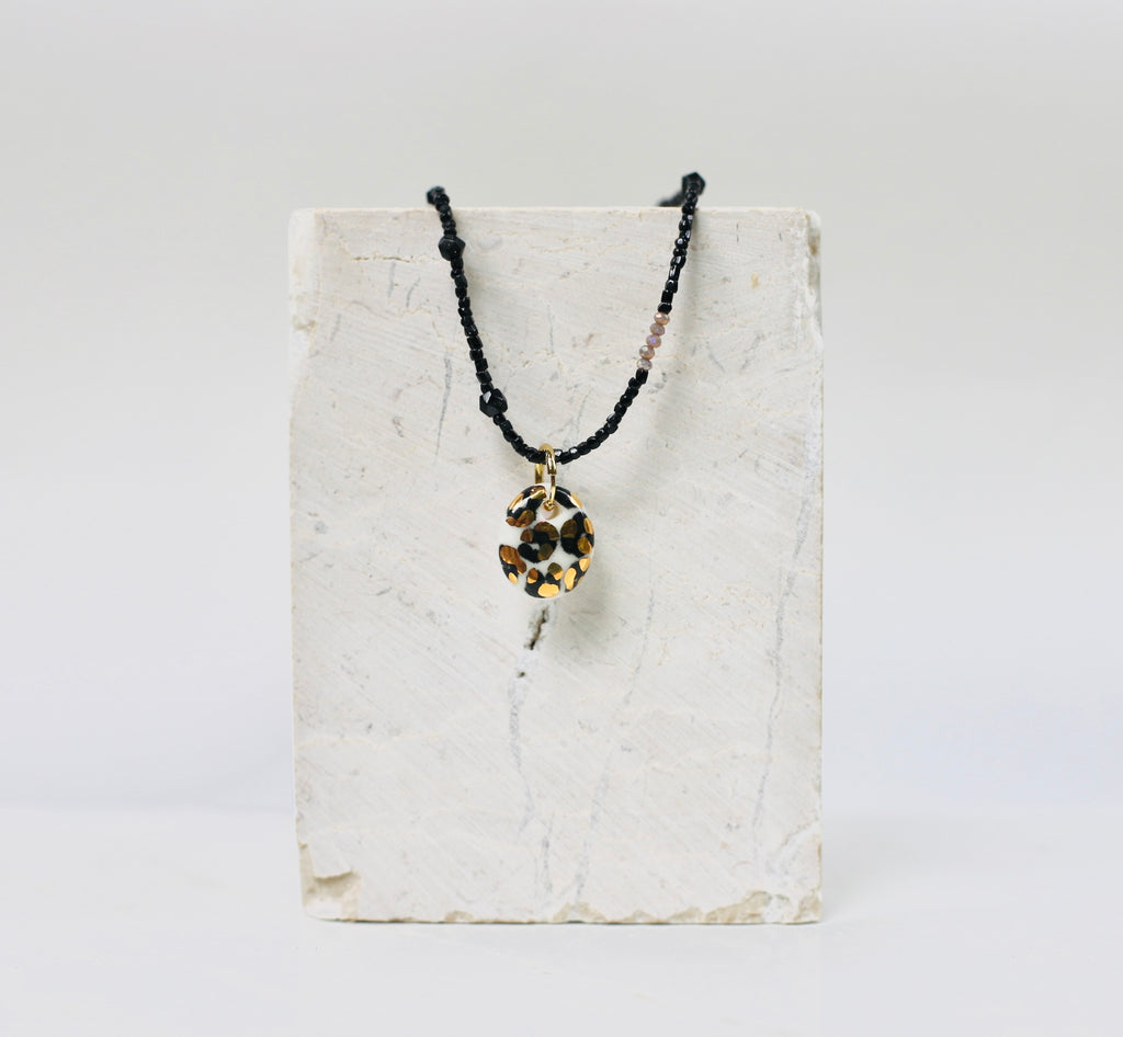 collier en petites perles noires mettant en valeur son médaillon rond en porcelaine au motif animalier léopard doré fait à la main 