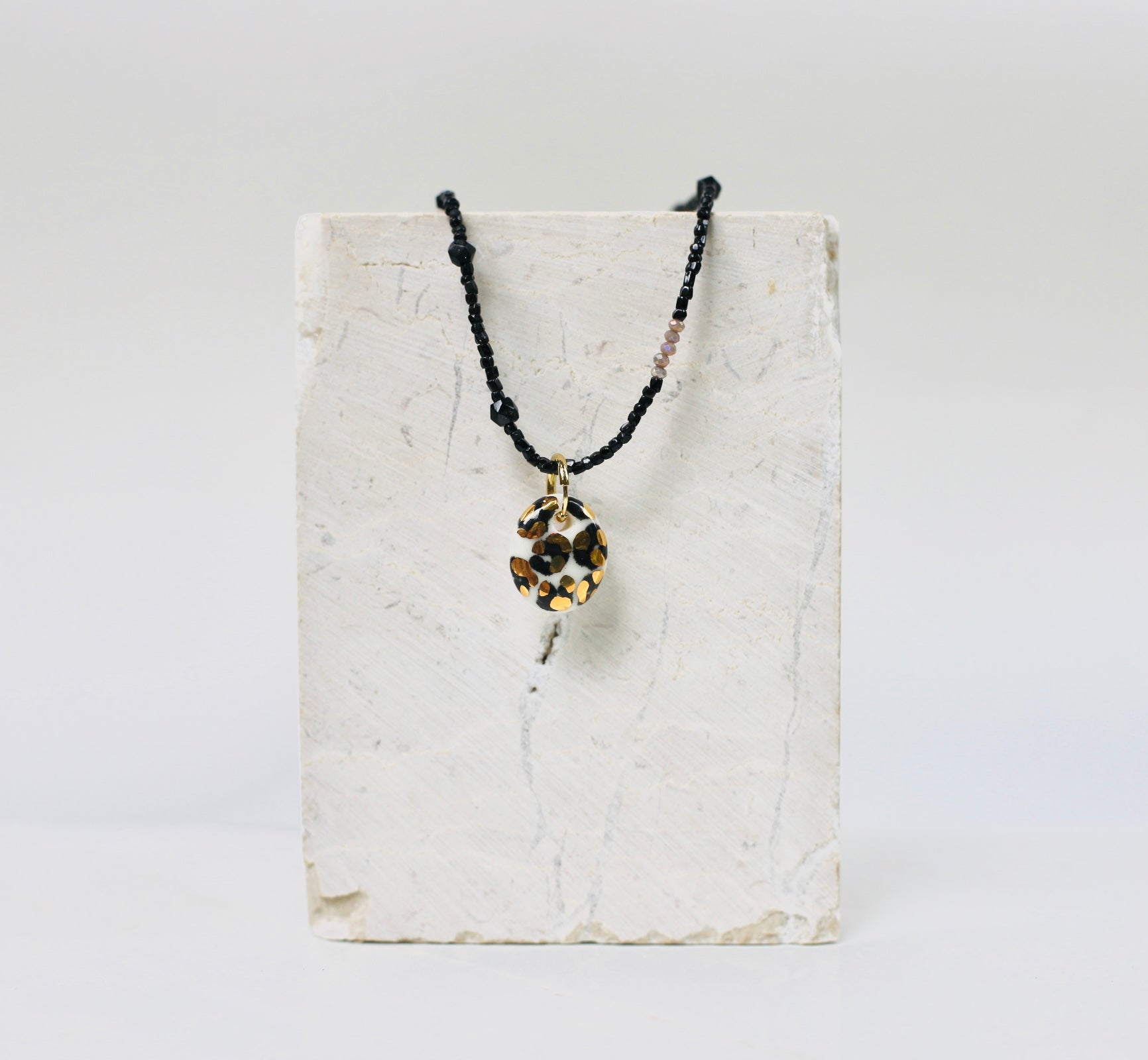 collier en petites perles noires mettant en valeur son médaillon rond en porcelaine au motif animalier léopard doré fait à la main 