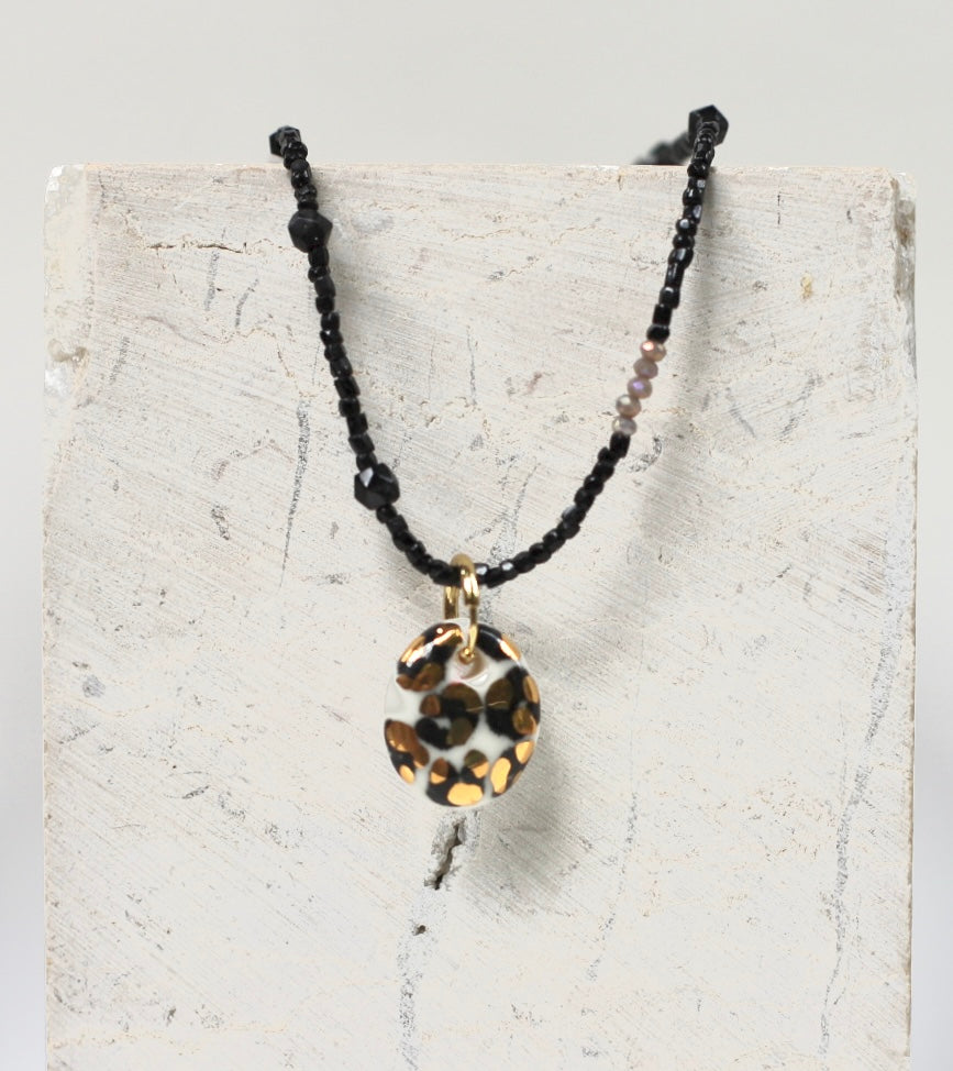 collier en fines perles noires orné d'un pendentif galet en porcelaine blanche avec un imprimé léopard tacheté noir et or fin fait main 