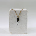 Collier pour femme avec une fine chaîne dorée à perles noires et un petit pendentif en porcelaine noire émaillée en forme de cœur ex-voto avec le mot FUCK écrit à l'or fin