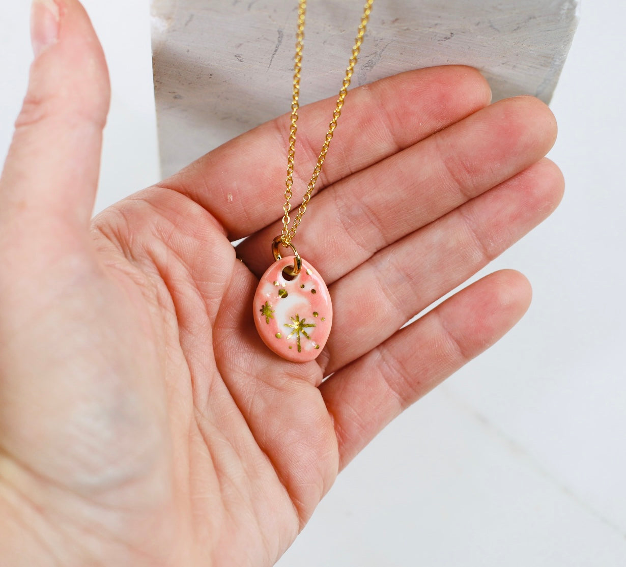 Collier fin doté d'une chaîne dorée et d'un pendentif à motif Lune en porcelaine rose saumon émaillée, et d'étoiles d'or fin fait à la main à Lyon 