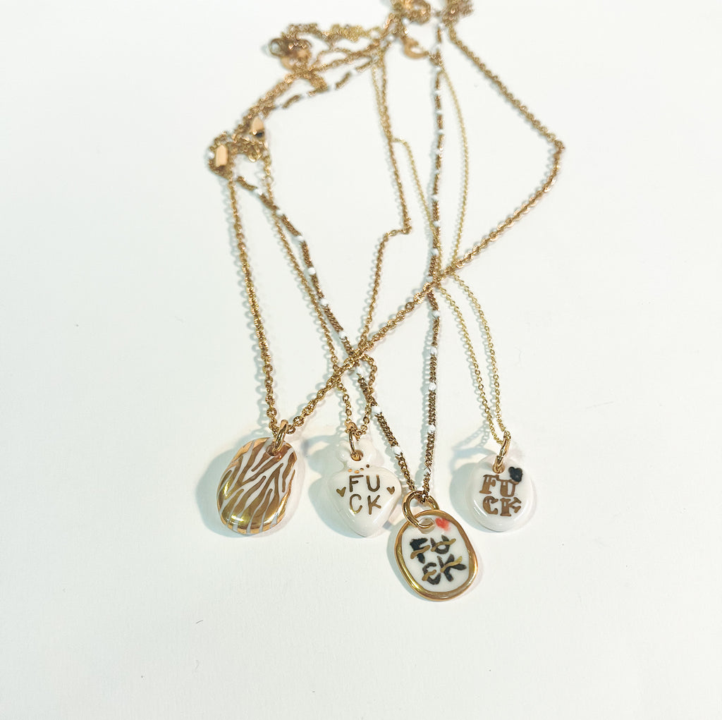 collier pendentif en porcelaine blanche orné de l'inscription FUCK calligraphiée en noir avec des détails et des contours à l'or fin fais main