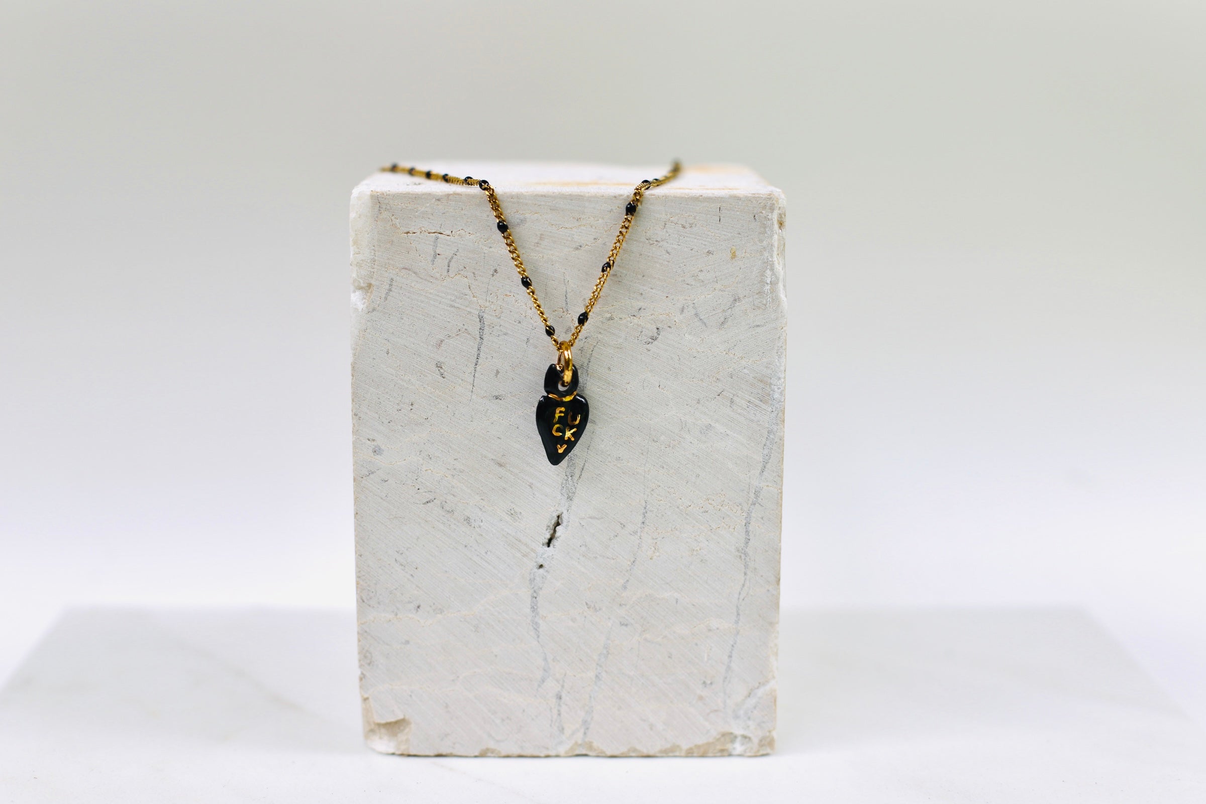 Collier délicat en or avec de mini perles noires et une petite médaille en porcelaine noire brillante en forme de cœur ex-voto aux inscriptions dorées.