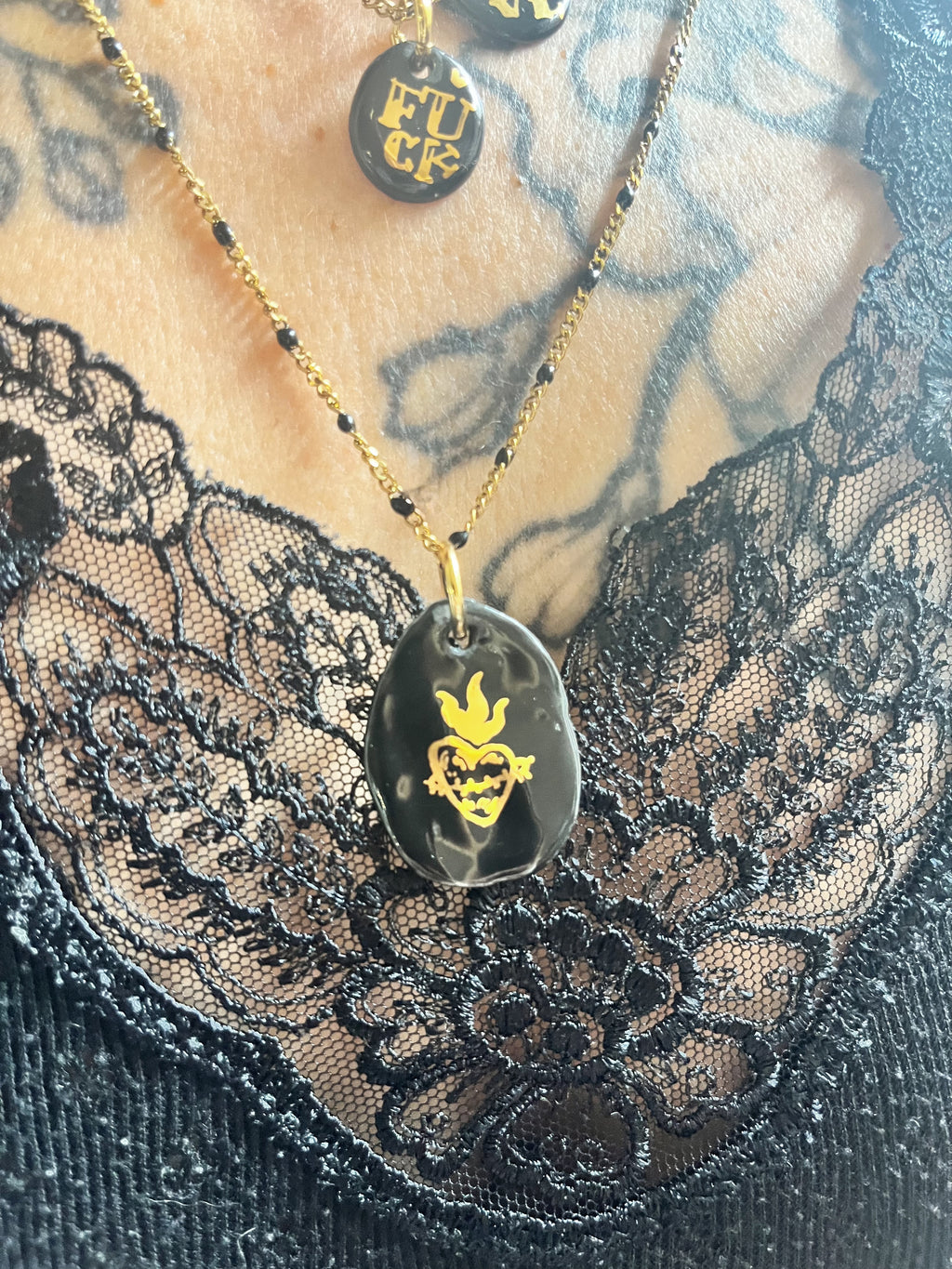 collier doté d'un médaillon galet en porcelaine noire brillante arborant un cœur ex-voto aux flammes dorées peintes à la main.