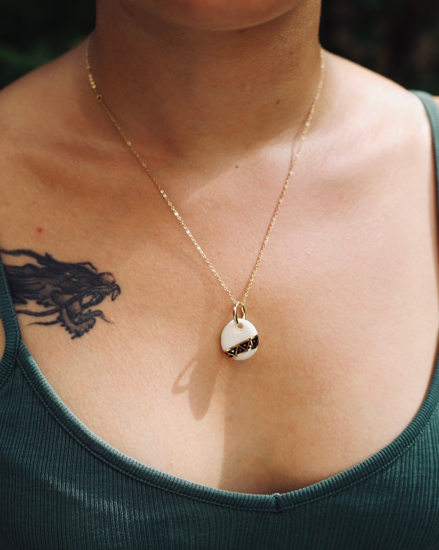 Collier avec un pendentif en porcelaine rond fabriqué à la main avec un motif art et déco en or liquide et noir peint à la main 