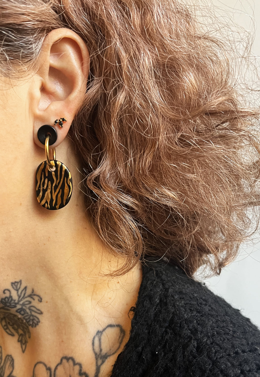 boucle d'oreille dorée composée d'un médaillon ovale en porcelaine noire avec un motif zébrées dorées peint à la main