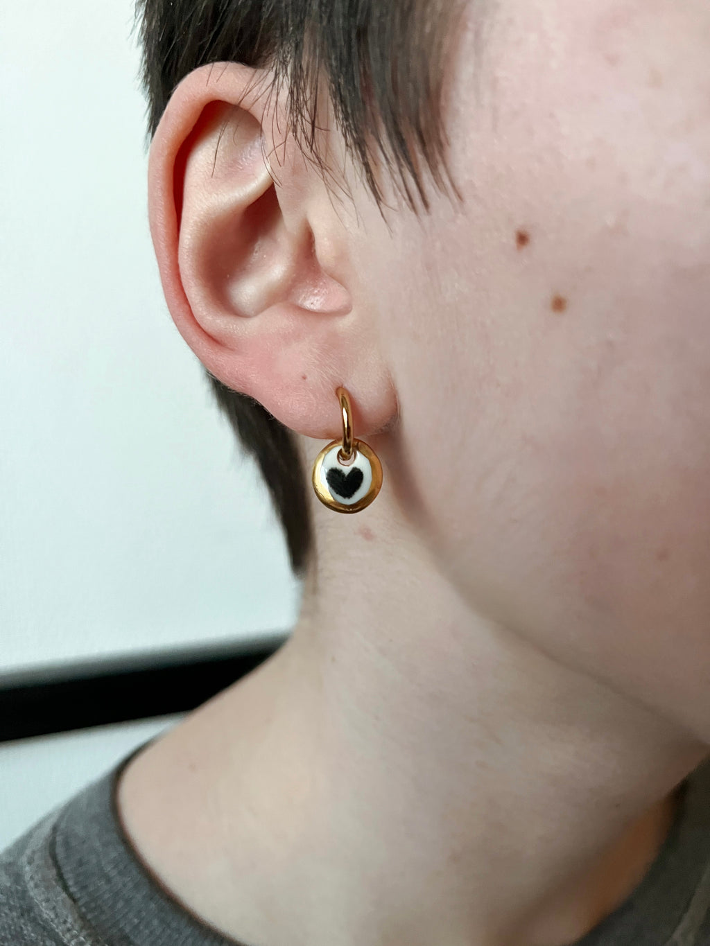 boucle d'oreille dorée avec petite médaille  en porcelaine blanche, avec un motif cœur noir entouré d'un liseré d'or fait à la main 