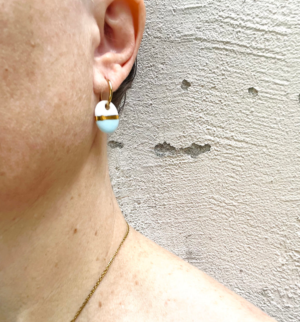 paire de boucles d'oreilles mini  dorées avec des pendentifs en porcelaine, moitié blanche et moitié bleu pastel, avec une touche d'or peinte à la main 