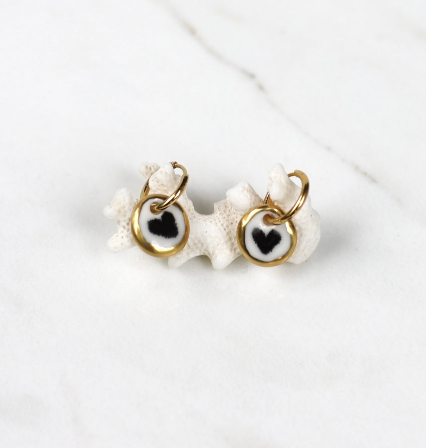 mini paire de boucles d'oreilles pendantes avec petit médaillons ronds en porcelaine blanche émaillée avec un motif cœur noir 