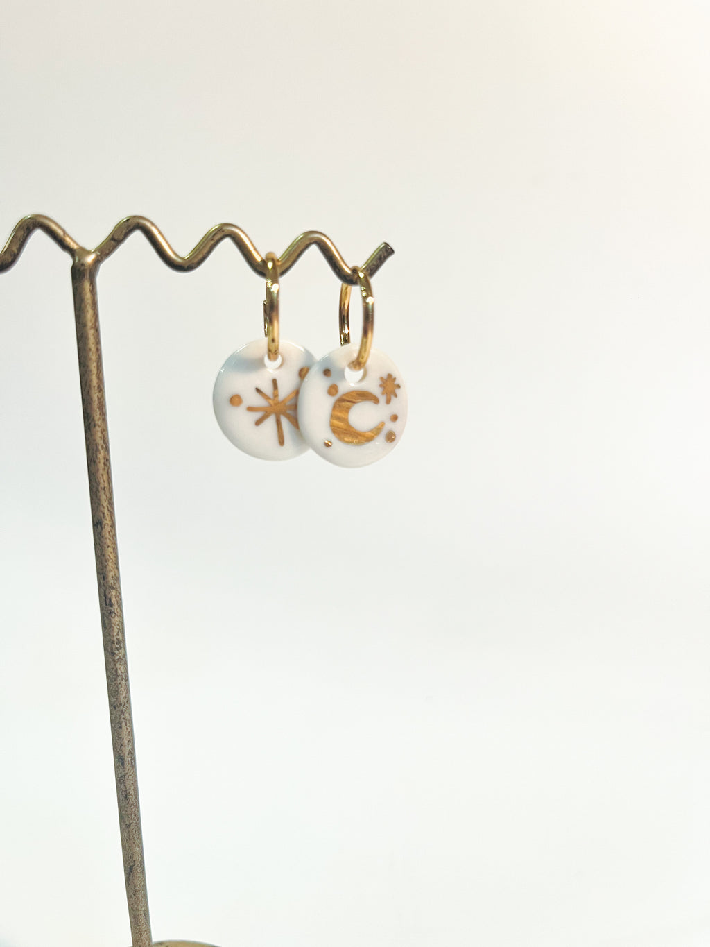 Paire de pendants d'oreilles célestes asymétriques avec leurs charms ronds en porcelaine blanche véritable, avec des motifs lune et étoile à l'or précieux.
