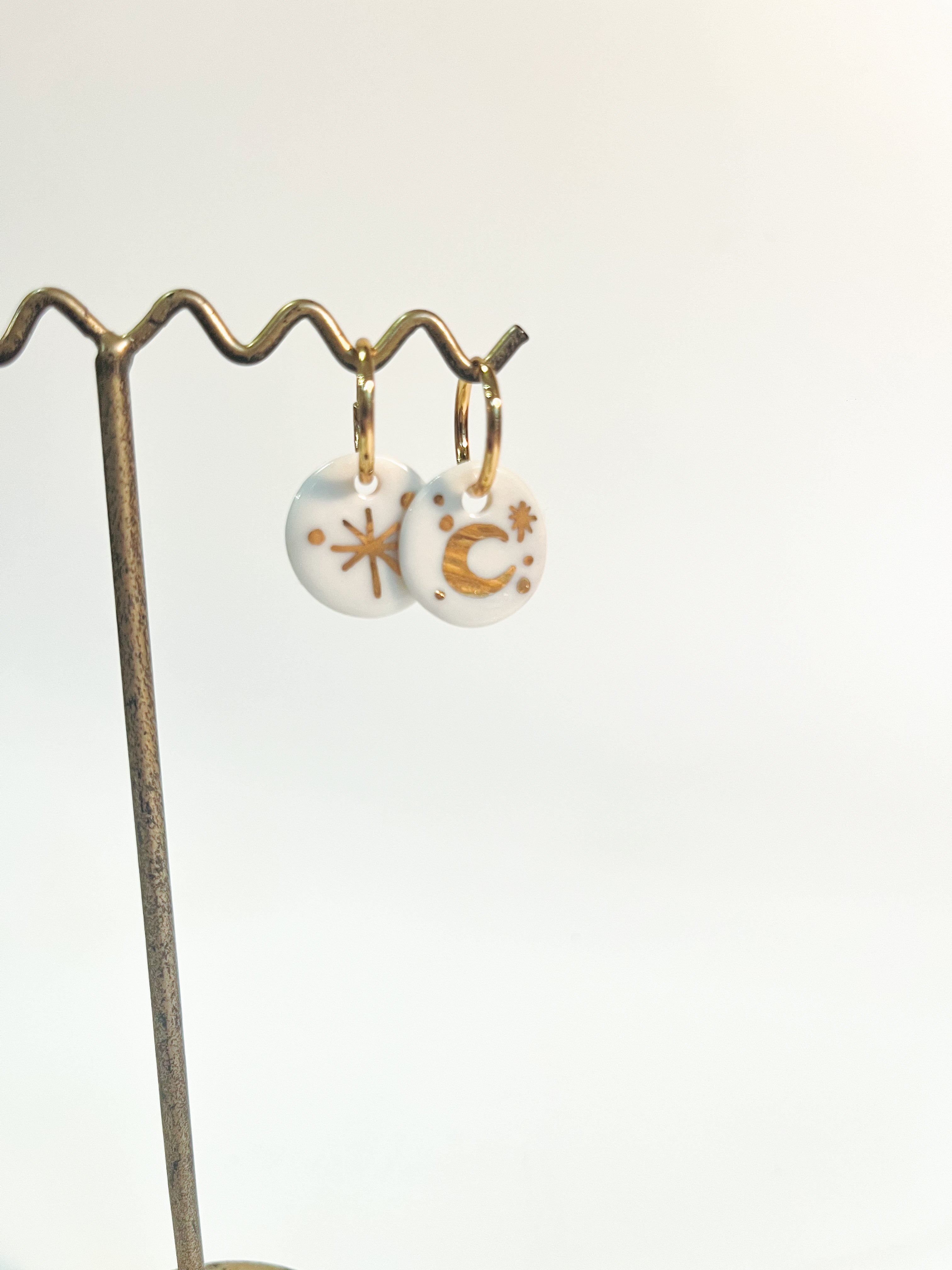 Paire de pendants d'oreilles célestes asymétriques avec leurs charms ronds en porcelaine blanche véritable, avec des motifs lune et étoile à l'or précieux.