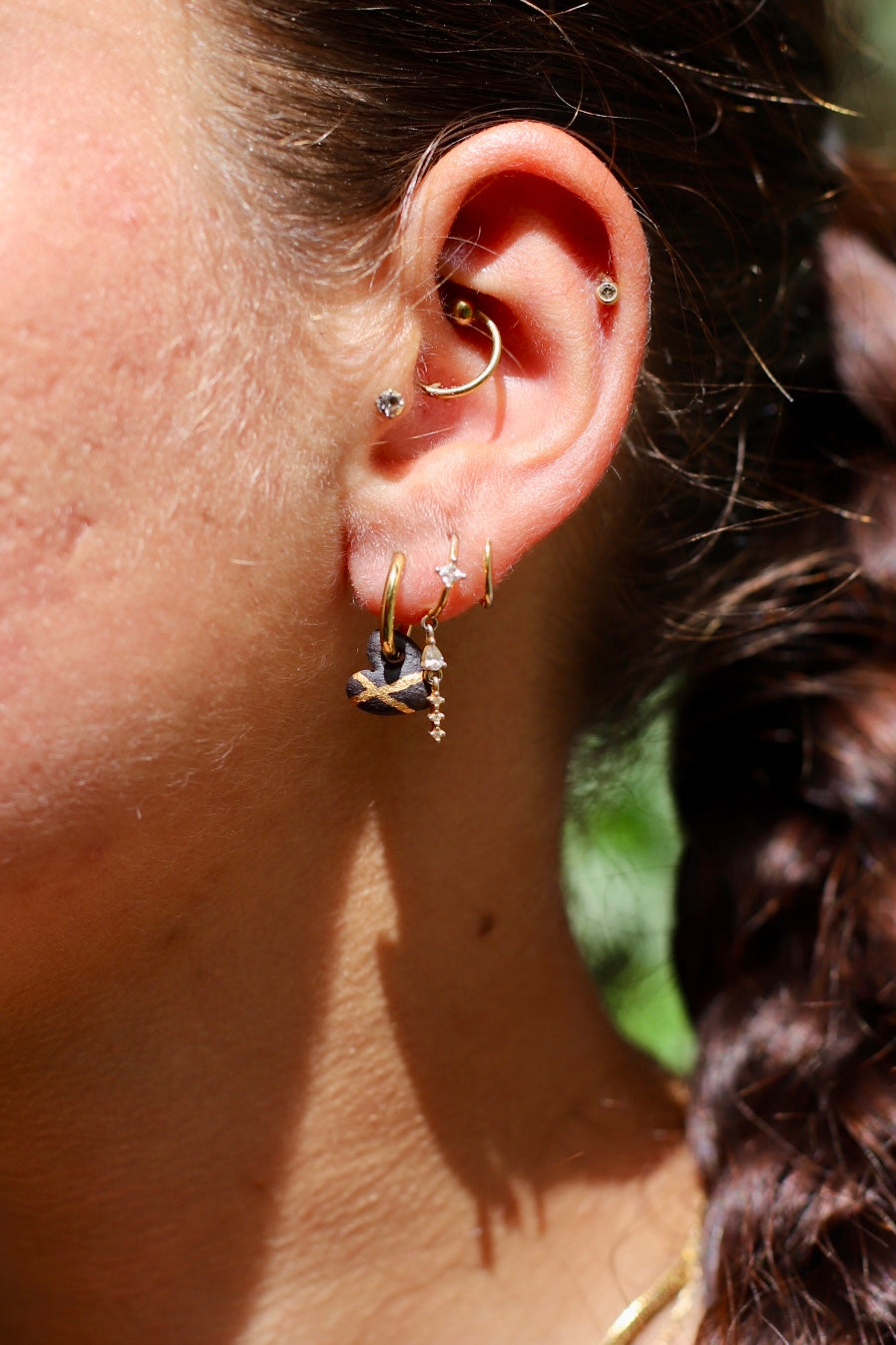 boucle d'oreille dorée avec son pendentif cœur en porcelaine matte noire, décoré de deux lignes graphiques croisées à l'or liquide fais à Lyon 