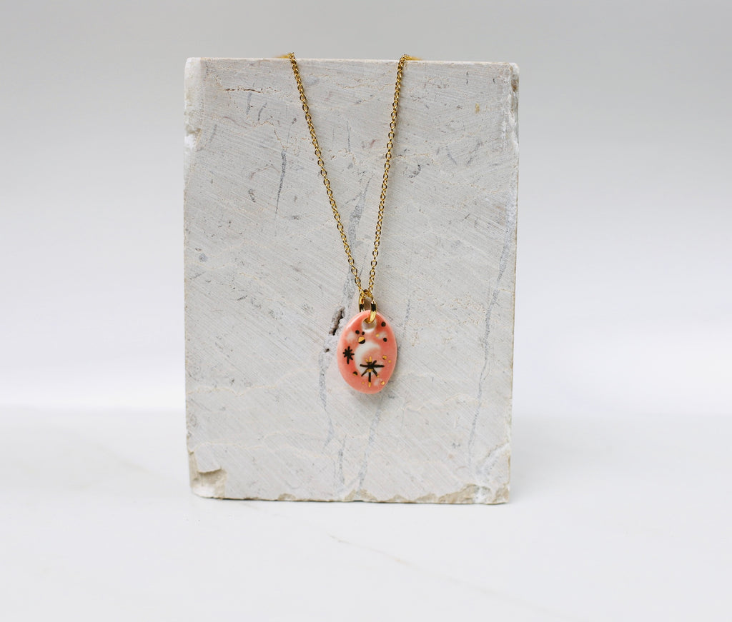 collier céleste en porcelaine rose avec des détail à l'or avec un motif lune peint à la main et des touches de noir. 