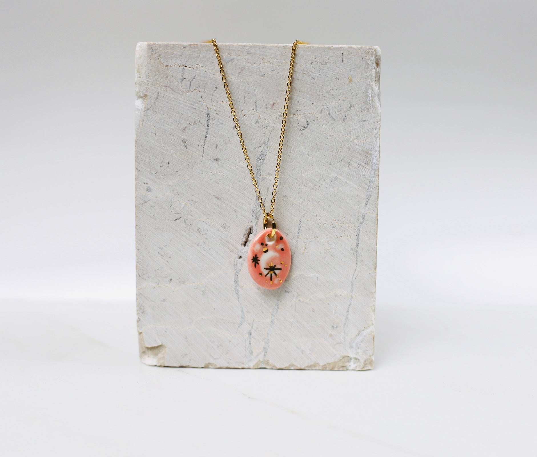 collier céleste en porcelaine rose avec des détail à l'or avec un motif lune peint à la main et des touches de noir. 