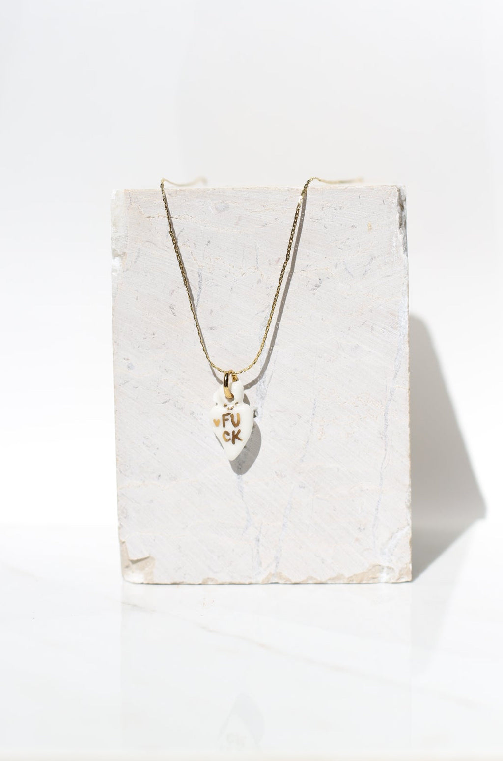 pendentif en porcelaine blanche en cœur ex-voto sacré avec 'inscription FUCK fait main à Lyon 