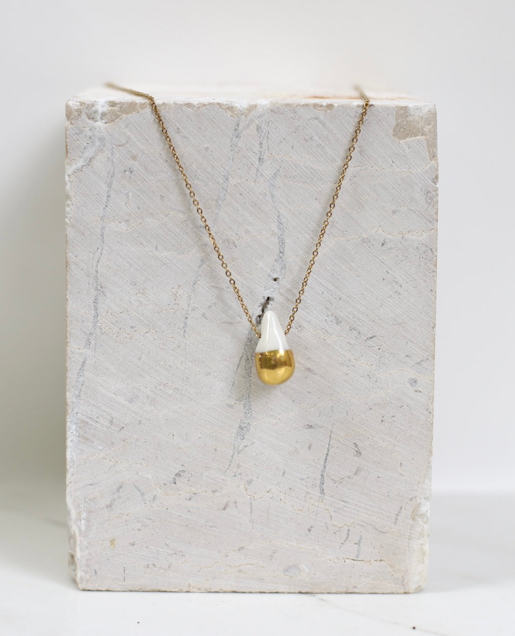 Pendentif délicat en forme de goutte d'eau en porcelaine blanche émaillée et dorée à l'or fin, suspendu à une fine chaîne dorée.