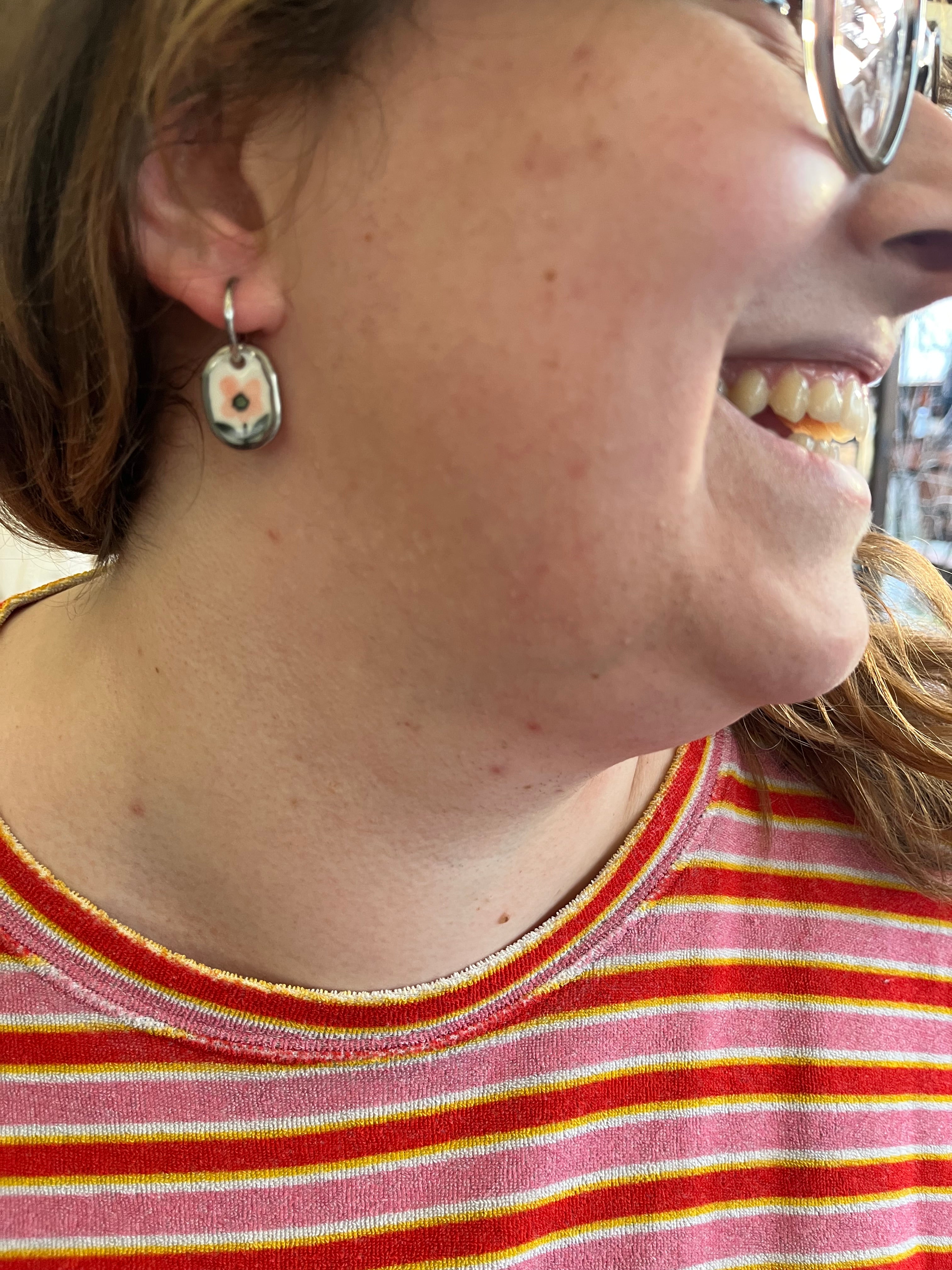 boucle d'oreille ovale en porcelaine, mettant en avant une fleur rose entourée d'un contour doré fait main.