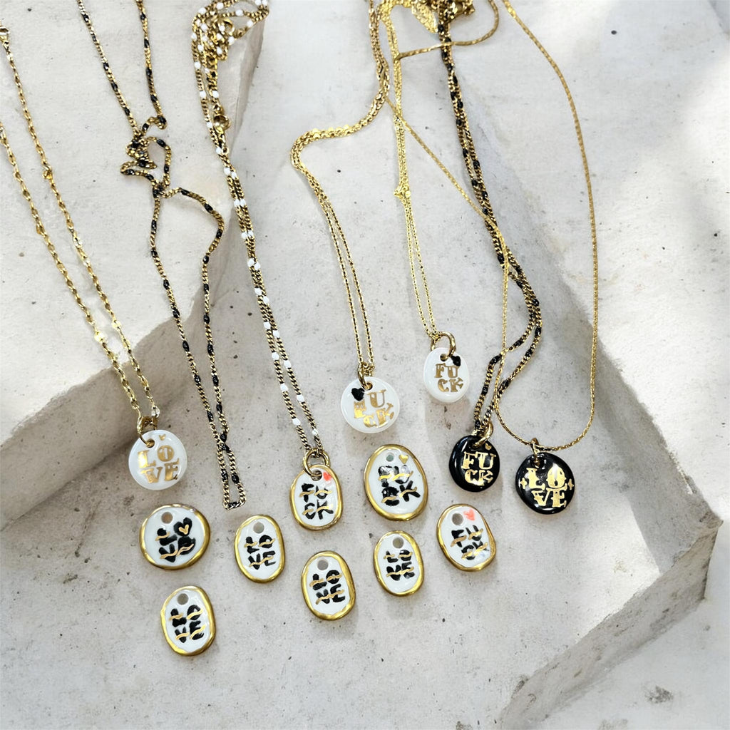 pendentifs ovales en porcelaine véritable avec le mot love peint à la main en noir, rehaussé de lignes d'or et d'une petite touche rouge.