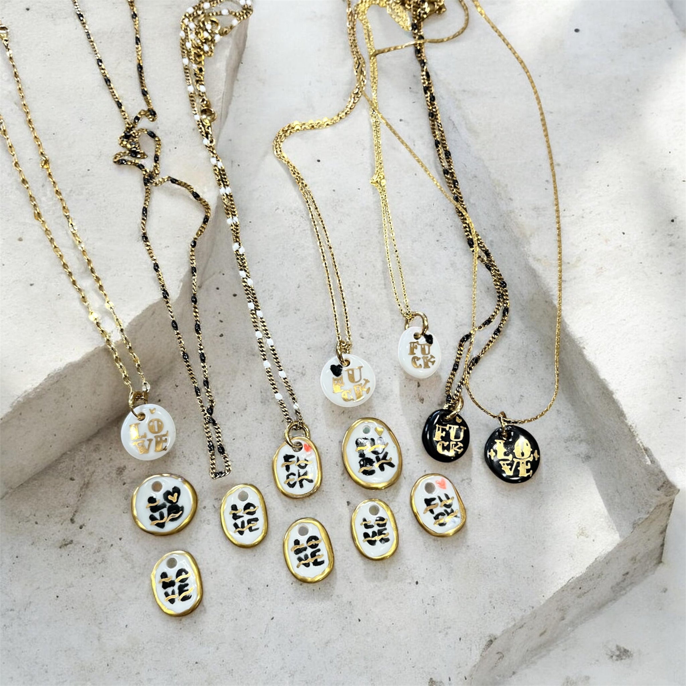pendentifs ovales en porcelaine véritable avec le mot love peint à la main en noir, rehaussé de lignes d'or et d'une petite touche rouge.