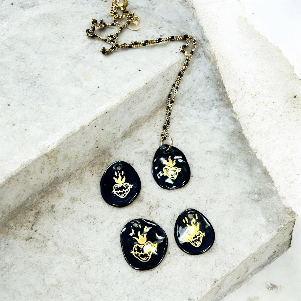 pendentifs galets en porcelaine noire émaillée, décoré à la main d'un motif sacré-cœur ex-voto flamboyant à l'or fin.