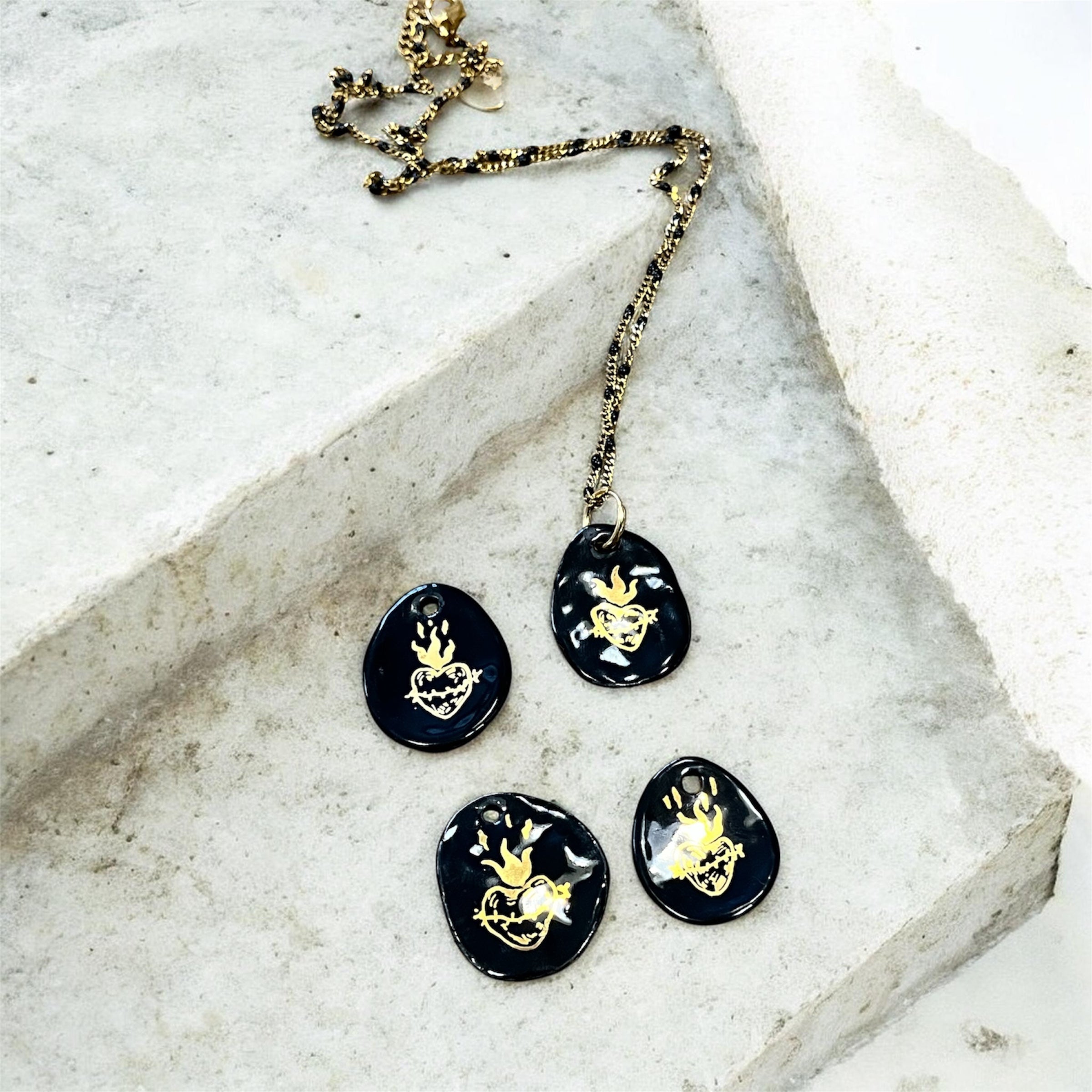 pendentifs galets en porcelaine noire émaillée, décoré à la main d'un motif sacré-cœur ex-voto flamboyant à l'or fin.