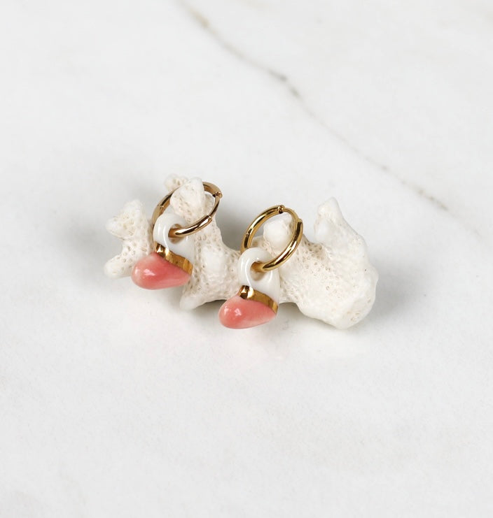 Paire de mini boucles d'oreilles pendantes pour femme composées de petits éléments organiques en porcelaine blanche et rose pastel, séparés par une ligne d'or fin brillant.
