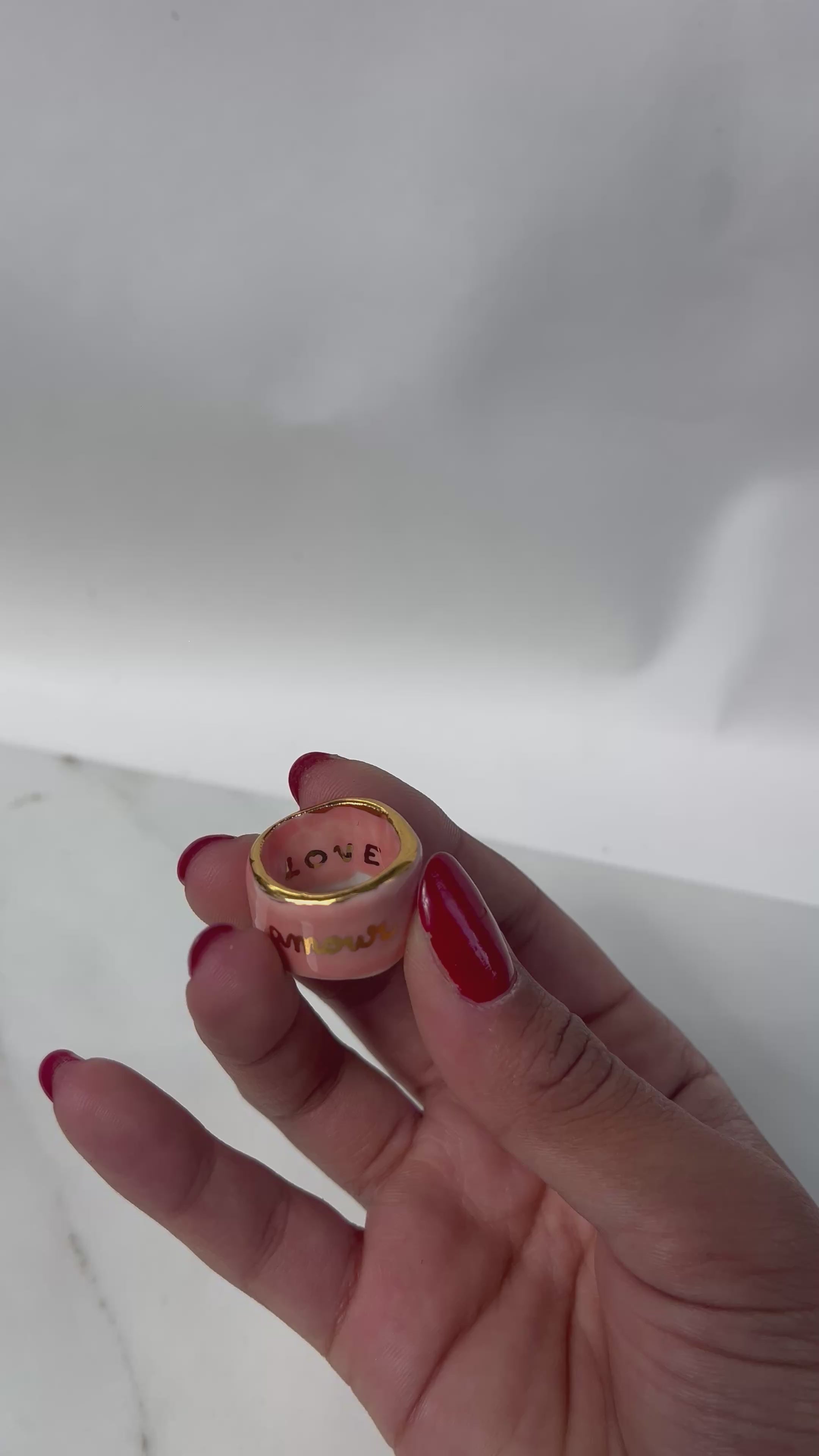 bague bandeau en porcelaine rose émaillée en taille 52 FR avec une inscription "amour" écrite ainsi qu'un œil protecteur dessiné à la main à l'or liquide.