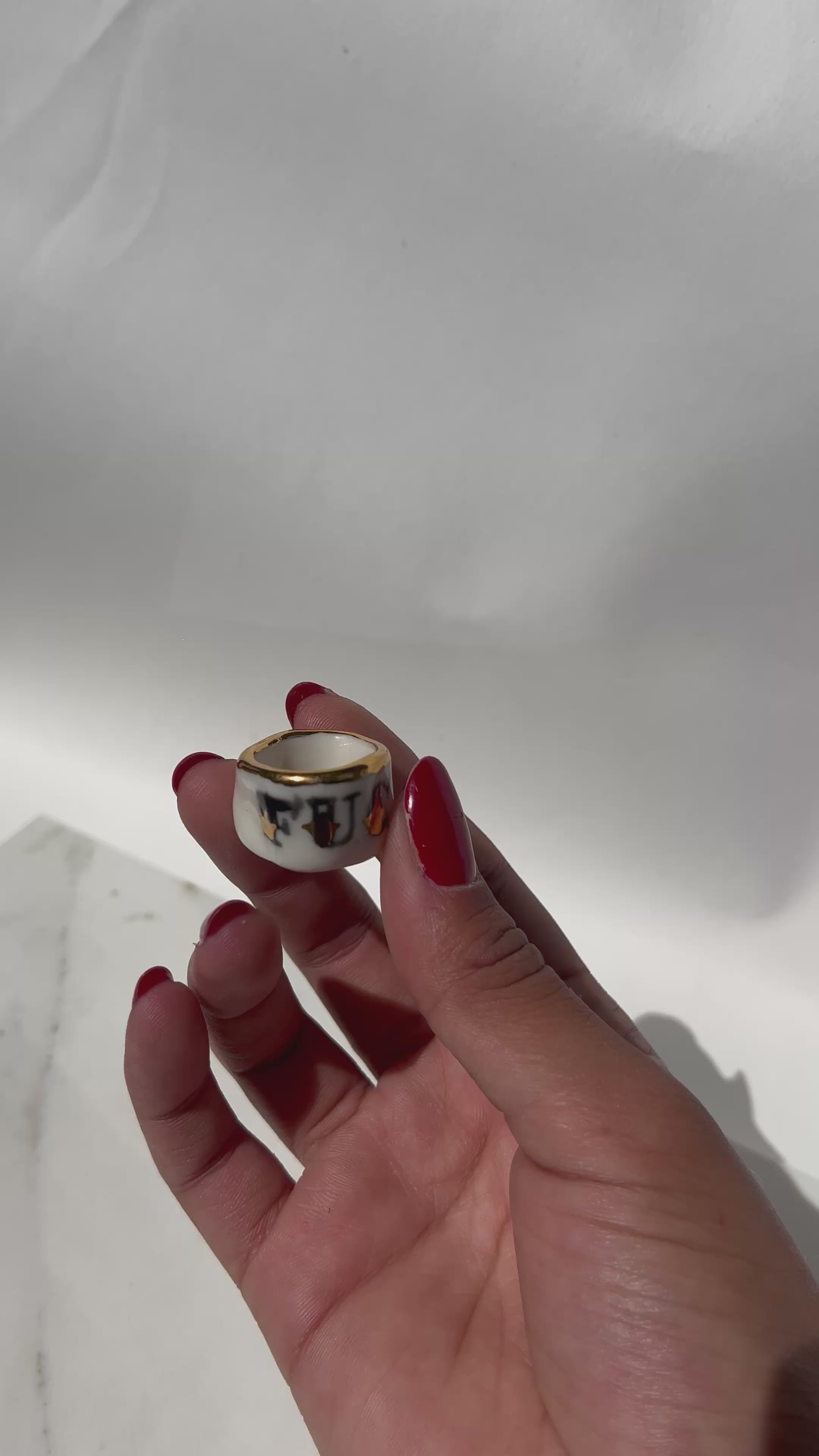 Bague type bandeau en porcelaine blanche émaillée en taille 53 FR avec un message FUCK ornées de petits motifs d'étoiles en or liquide peintes à la main.